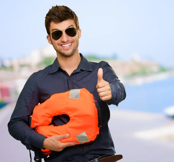 Hombre de pie sosteniendo chaleco salvavidas mostrando pulgares hacia arriba — Foto de Stock