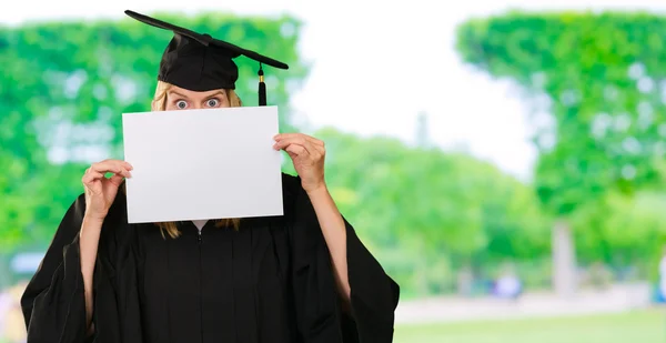 Graduate kvinna gömmer sig bakom ett tomt papper — Stockfoto