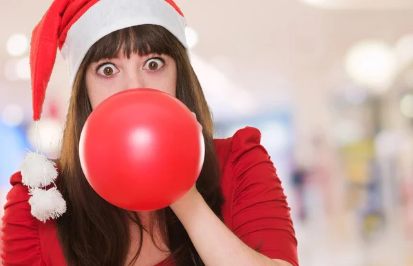 Frau bläst Luftballon und trägt Weihnachtsmütze — Stockfoto