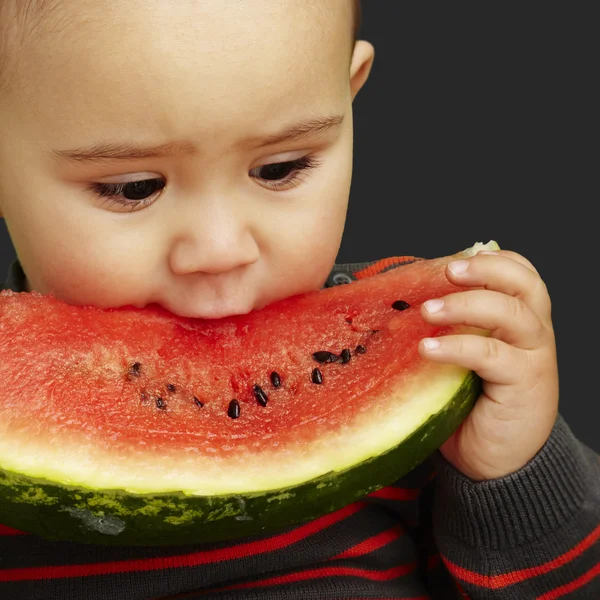 Porträt eines hübschen Kindes, das eine Wassermelone über einem schwarzen Backgr beißt — Stockfoto