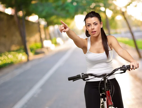 Молодая девушка сидит на велосипеде указывая — стоковое фото
