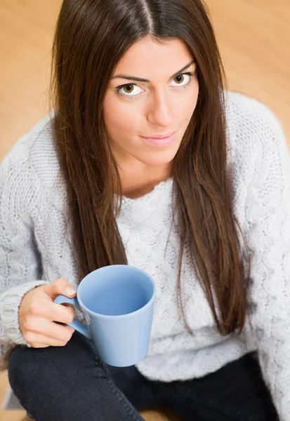 Woman sitting on the floor while looking up and holding a mug — Stock Photo, Image