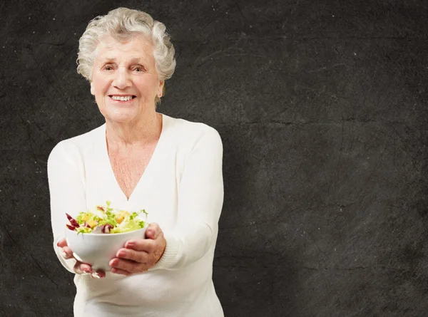 Portrait d'une femme âgée montrant une salade fraîche contre un grunge — Photo