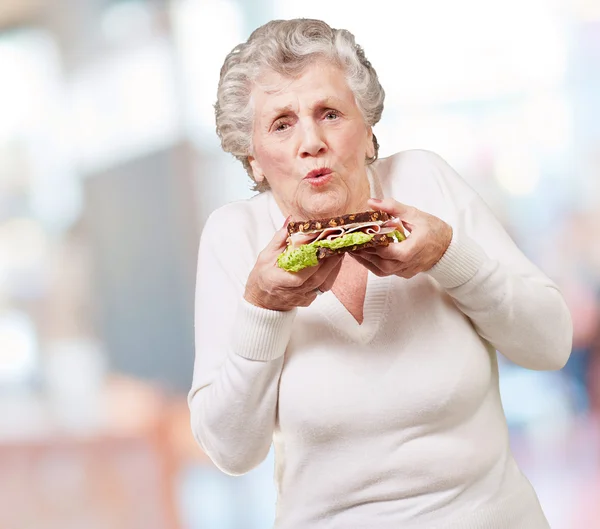 Retrato de mulher idosa segurando um delicioso sanduíche interior — Fotografia de Stock