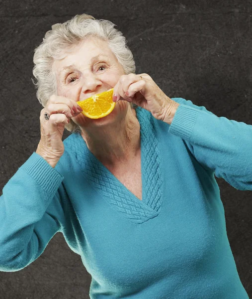 Retrato de mulher idosa segurando uma fatia de laranja na frente dela — Fotografia de Stock