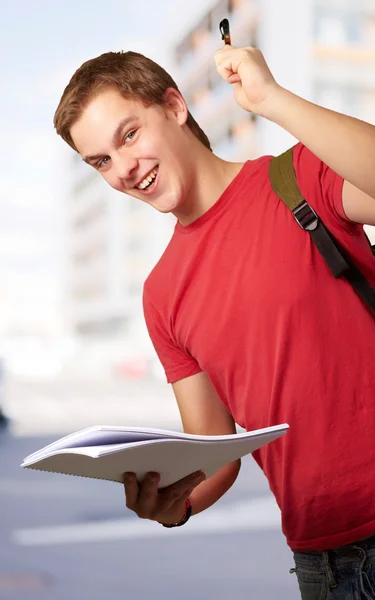 Portrait d'un bel étudiant tenant un cahier et un stylo contre un — Photo