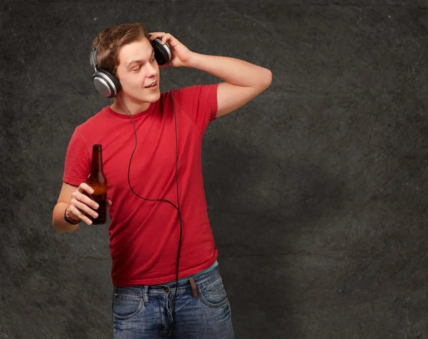 Portrait de jeune homme écoutant de la musique et tenant de la bière contre un — Photo