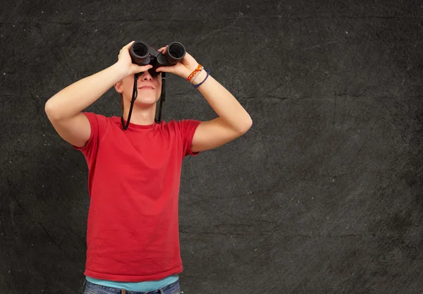 Portrait of young man with binoculars against a grunge wall — Stock Photo, Image