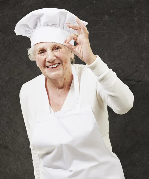 Senior woman cook doing an excellent symbol against a grunge bac Royalty Free Stock Photos