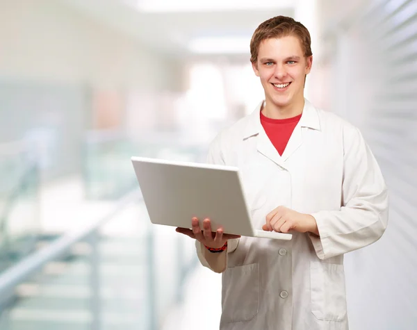 Portret van een jonge student met laptop bij ingang van gebouw Stockfoto