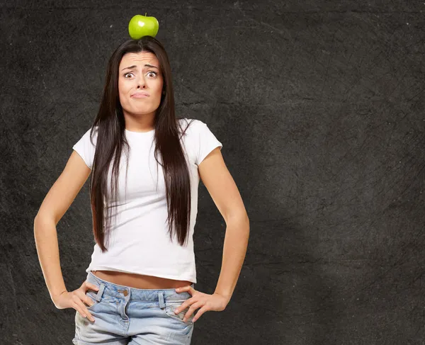 Πορτραίτο νεαρής γυναίκας κρατώντας πράσινο μήλο στο κεφάλι της κατά — Φωτογραφία Αρχείου