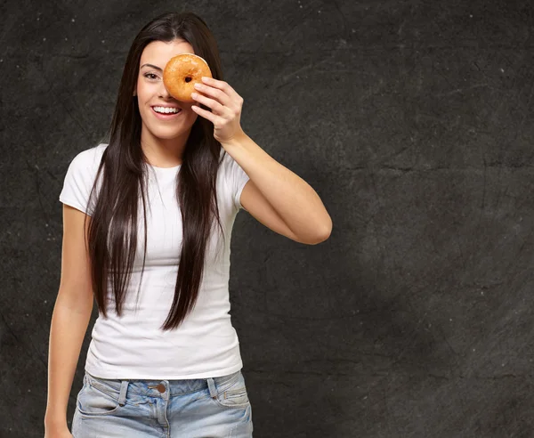 Portret van een jonge vrouw op zoek via een donut tegen een grunge — Stockfoto