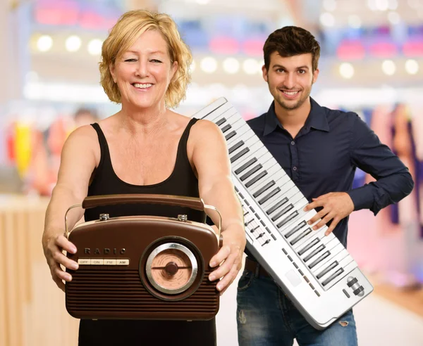 Kobieta trzyma radia infront człowieka posiadającego fortepian — Zdjęcie stockowe