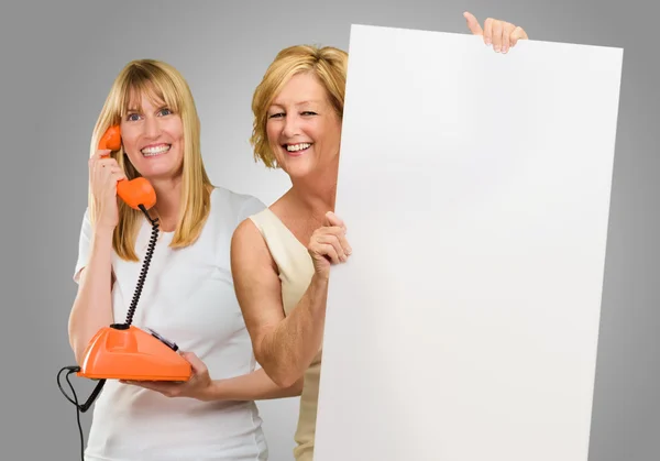 Vrouw met plakkaat terwijl andere vrouw praten over telefoon — Stockfoto