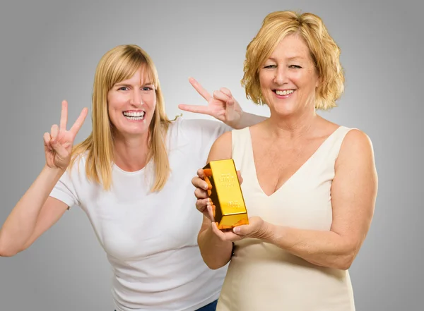 Mujer sosteniendo la barra de oro mientras que otra mujer gestos detrás —  Fotos de Stock