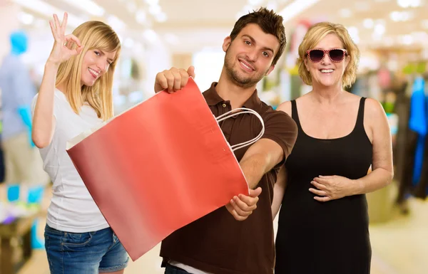 Homem segurando saco de compras na frente de duas mulheres felizes — Fotografia de Stock