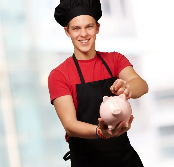 Male chef holding a piggybank and a coin — Stock Photo, Image