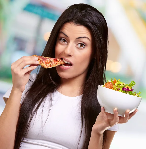 Frau isst ein Stück Pizza und hält eine Salatschüssel in der Hand — Stockfoto