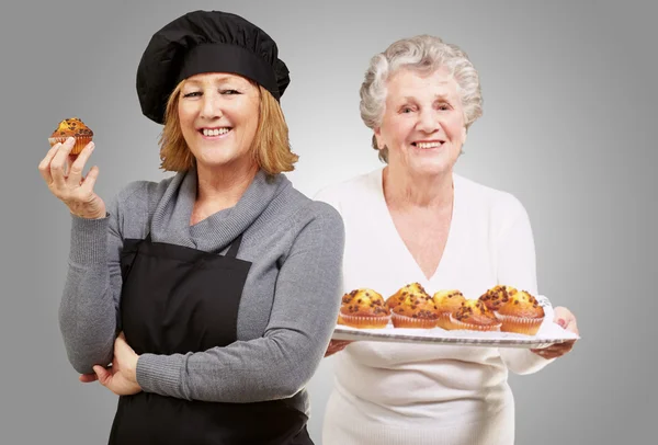 Kvinnliga kock hålla muffins i främre äldre kvinna — Stockfoto