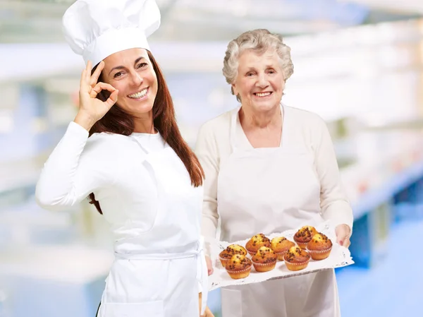 Deux joyeuses cuisinières présentant des muffins — Photo