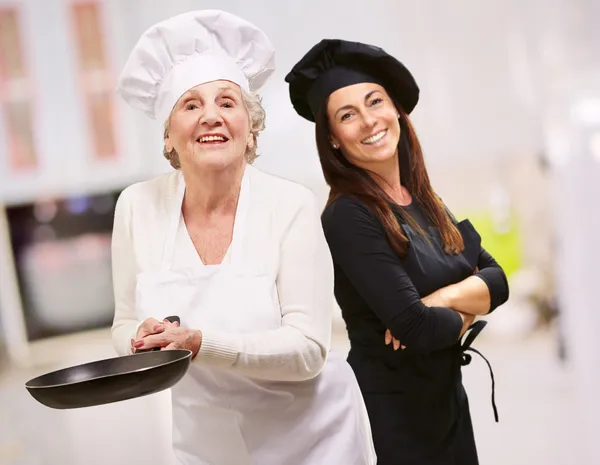 Ανώτερος σεφ κρατώντας το τηγάνι μπροστά από το χαμογελαστό γυναίκα — Φωτογραφία Αρχείου