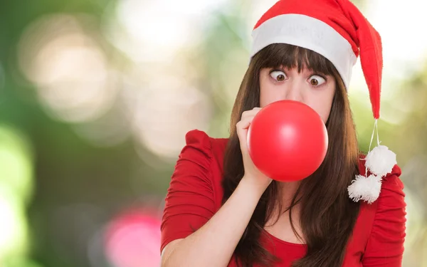 Рождественская женщина, надувающая воздушный шар с скрещенными глазами — стоковое фото