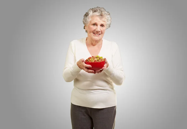 Portrait of healthy senior woman holding cereals bowl over grey — Stock Photo, Image