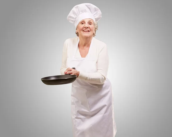 Retrato de um cozinheiro amigável mulher sênior segurando pan sobre cinza b — Fotografia de Stock