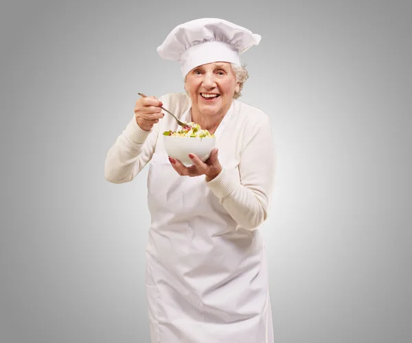 Retrato de cocinera senior comiendo ensalada sobre gris — Foto de Stock