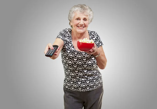 Retrato de mulher idosa feliz olhando a tv sobre backgrou cinza — Fotografia de Stock