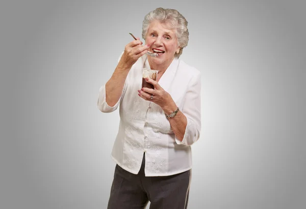 Retrato de mulher idosa comendo chocolate e xícara de creme sobre o gre — Fotografia de Stock