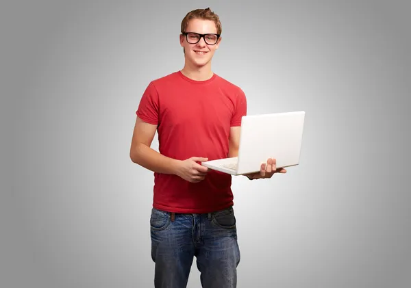 Retrato de un joven estudiante sosteniendo el ordenador portátil sobre fondo gris —  Fotos de Stock