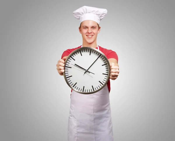 Retrato de jovem cozinheiro segurando relógio sobre fundo cinza — Fotografia de Stock