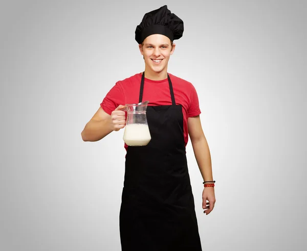 Portrait of young cook man holding milk jar over grey background — Stock Photo, Image