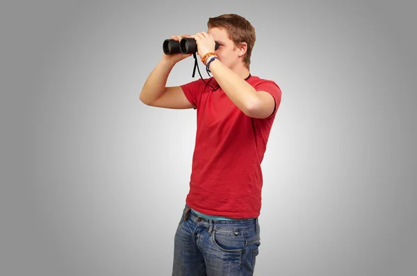 Portret van jonge man kijkend door een verrekijker over grijs bac — Stockfoto