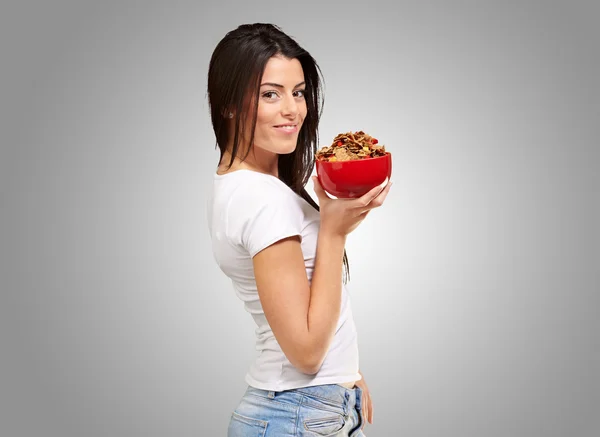 Retrato de mujer joven sosteniendo un tazón de cereal sobre fondo gris —  Fotos de Stock