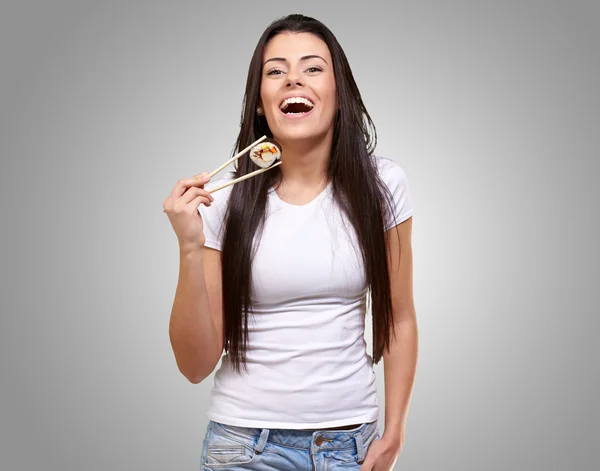 Portrait of young woman holding sushi against a grey background — Stock Photo, Image