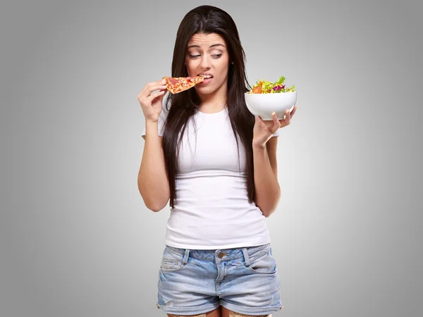 Portrait de jeune femme mangeant de la pizza et regardant la salade sur gris — Photo