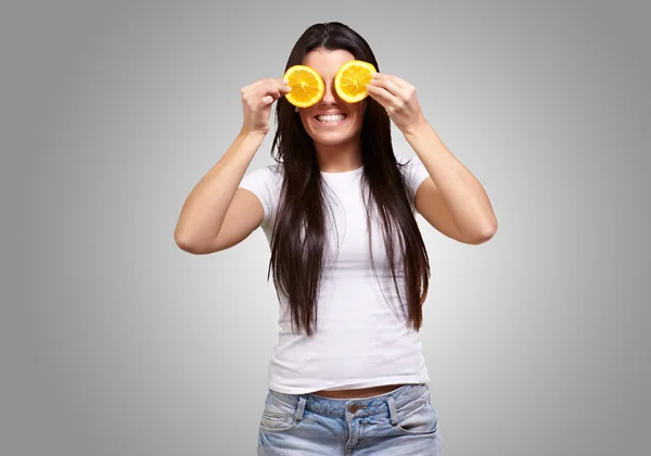 Portrait of young woman holding orange slices in front of her ey — Stock Photo, Image