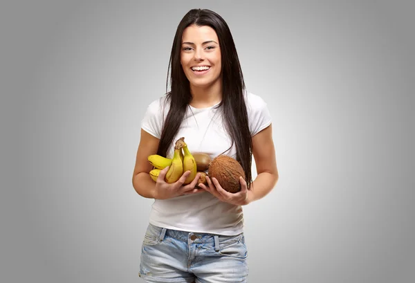 Portrait de jeune femme tenant des fruits tropicaux contre un b gris — Photo