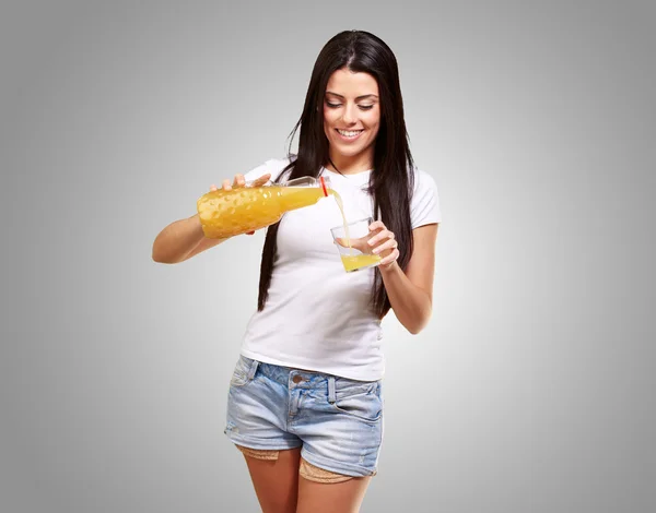 Retrato de jovem derramando suco de laranja em vidro sobre cinza — Fotografia de Stock