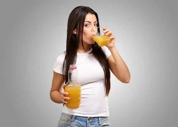 Retrato de menina bebendo suco de laranja contra uma parte traseira cinza — Fotografia de Stock