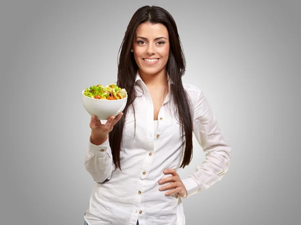 Portret van een jonge vrouw met salade over grijs — Stockfoto