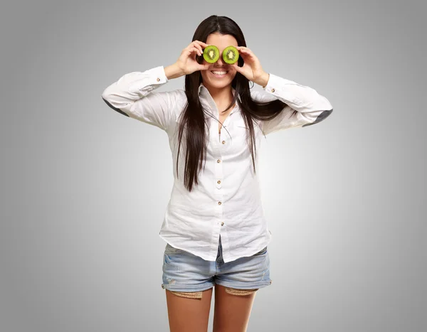 Portrait of young girl holding kiwi slices in front of her eyes — Stock Photo, Image