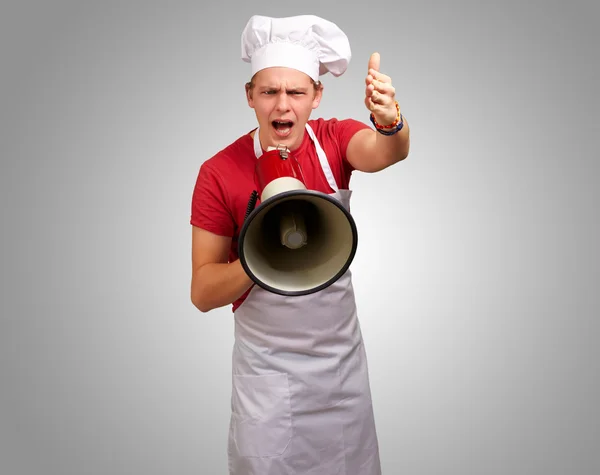 Portrait of young cook man screaming with megaphone and gesturin Stock Image