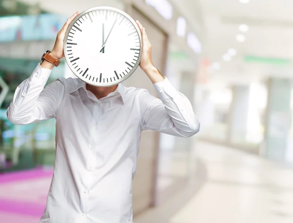 Joven sosteniendo un gran reloj cubriendo su rostro — Foto de Stock