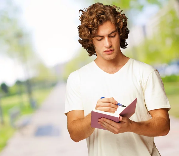 Een jonge man schrijven op een notitieblok — Stockfoto