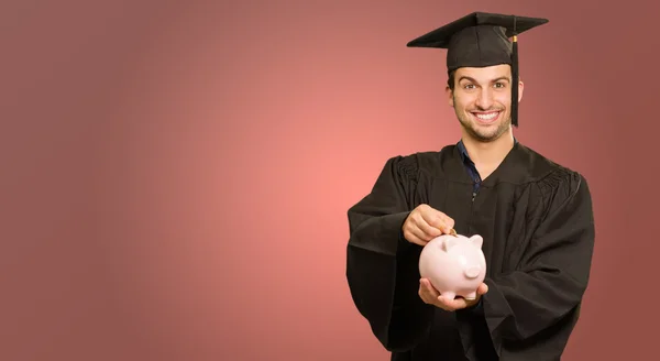 Graduate Man Inserindo Moeda Em Piggybank — Fotografia de Stock