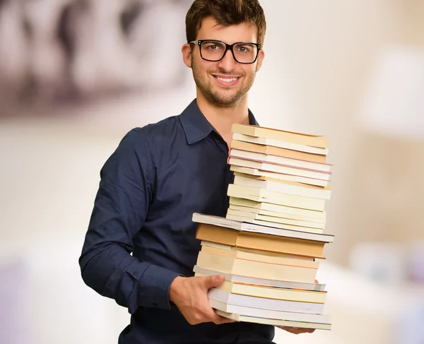 Młody człowiek szczęśliwy, trzymając stos książek — Zdjęcie stockowe