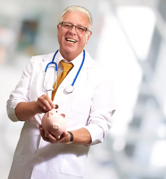 Médico masculino poniendo monedas en una alcancía —  Fotos de Stock